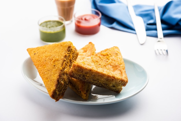 Pain de mie Pakora ou pakoda en forme de triangle servi avec du ketchup aux tomates, chutney vert, collation indienne populaire à l'heure du thé