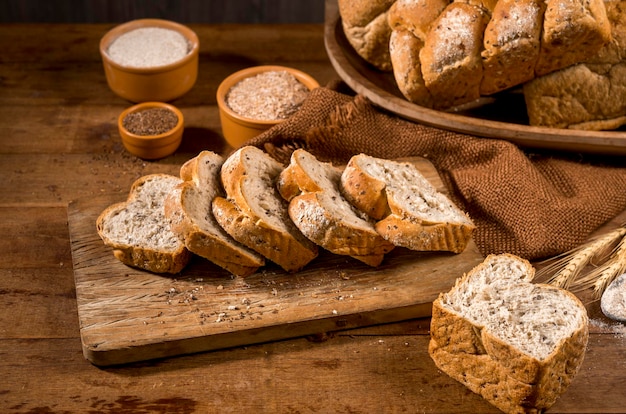 Pain de mie tranché à base de graines de sésame ( gergelim ) sur une table en bois rustique avec d'autres pains et ingrédients en arrière-plan.