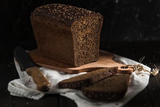 Pain noir aux graines de cumin, des tranches reposent sur une planche de bois