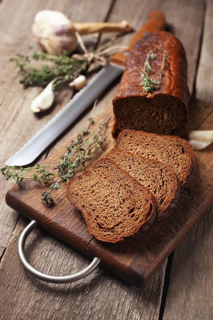 Pain noir sur une planche à découper en bois avec des herbes.