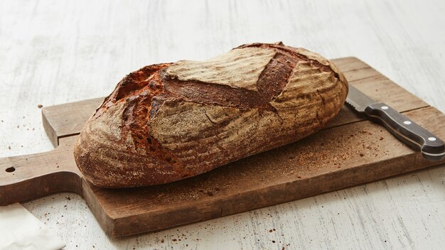 Pain ovale de seigle sur une planche à découper avec un couteau sur fond blanc