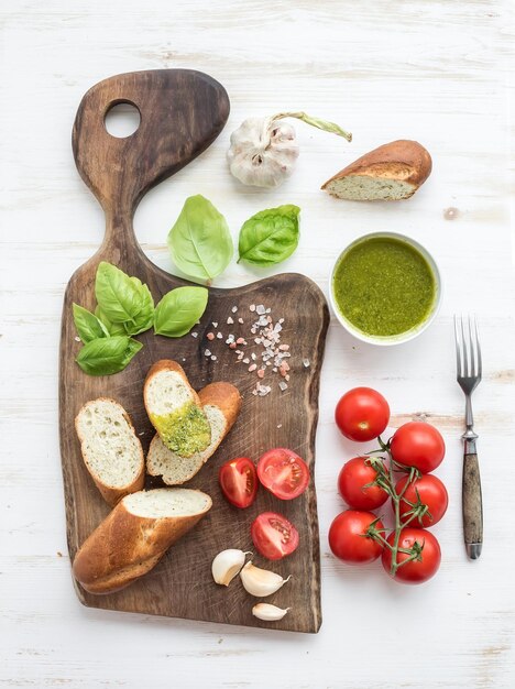 Pain sauce pesto tomates cerises basilic frais et ail sur planche à découper en noyer rustique sur fond de bois blanc