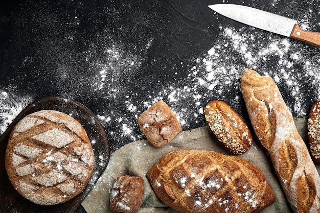 Pain de seigle fait maison saupoudré de farine et de diverses céréales et graines sur fond noir avec des pointes...