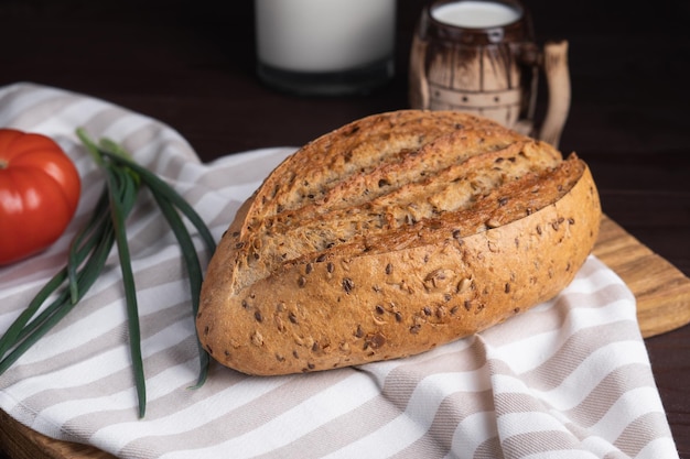 Pain de seigle frais fait maison tas de tomates tasse d'argile d'oignon et bouteille de lait sur une planche à découper en bois