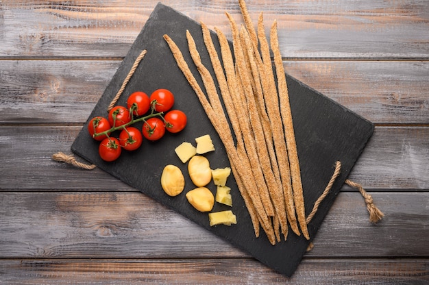 Pain De Seigle Grissini, Tomates Cerises, Fromage Et Légumes Verts Sur Une Planche En Fonte Noire Sur Un Fond En Bois.