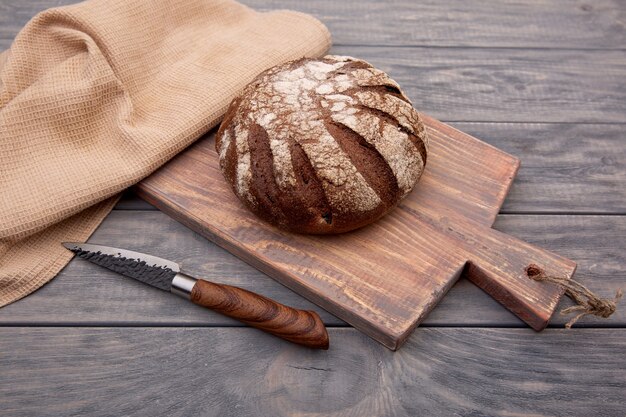 Pain de seigle pain rond sur une planche de bois avec un couteau en bois rustique. Vue de dessus.