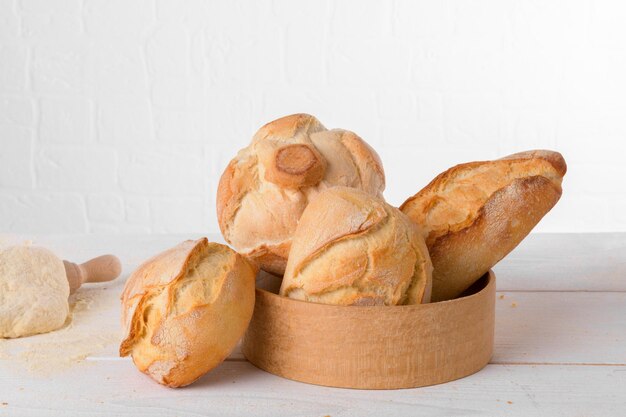 Pains de blé italiens frais dans le tamis sur la table avec de la farine et de la pâte sur fond blanc