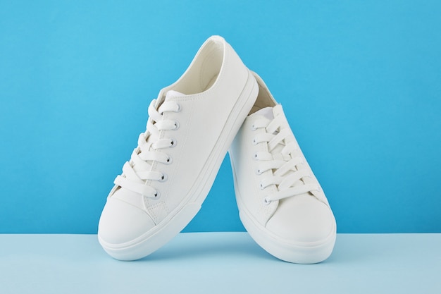 Paire de baskets blanches élégantes à la mode, chaussures de sport de course sur fond bleu pastel.