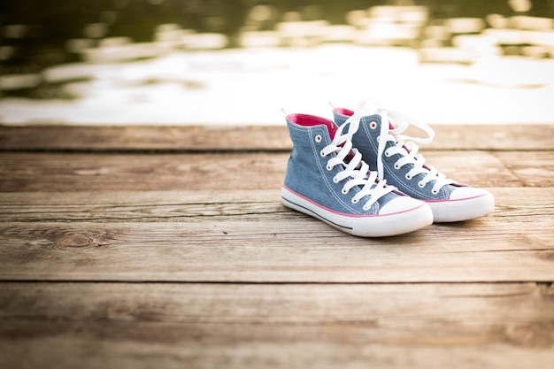 Paire de baskets jeans debout sur une jetée en bois sur le fond de l'eau