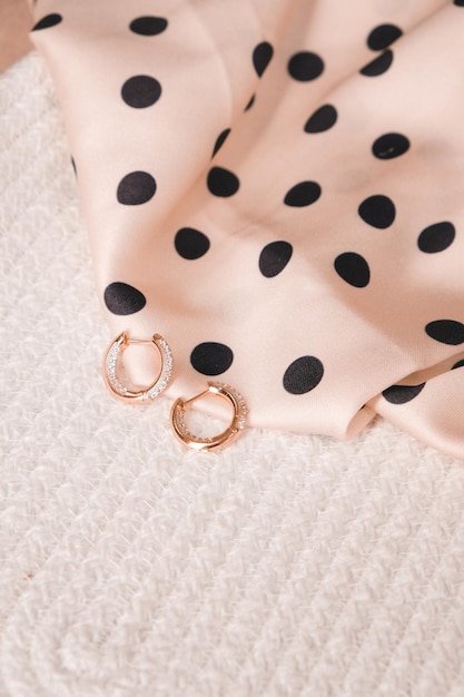 Une paire de boucles d'oreilles créoles dorées sur une robe rose à pois.