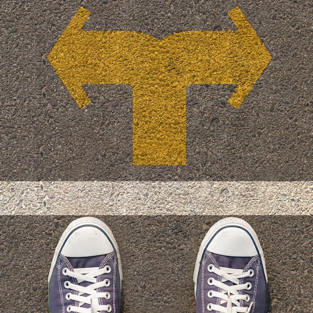 Photo paire de chaussures debout sur une route avec une flèche jaune à double sens