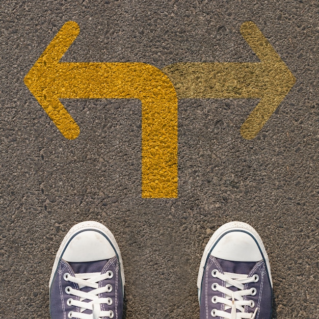 Photo paire de chaussures debout sur une route avec une flèche jaune à double sens