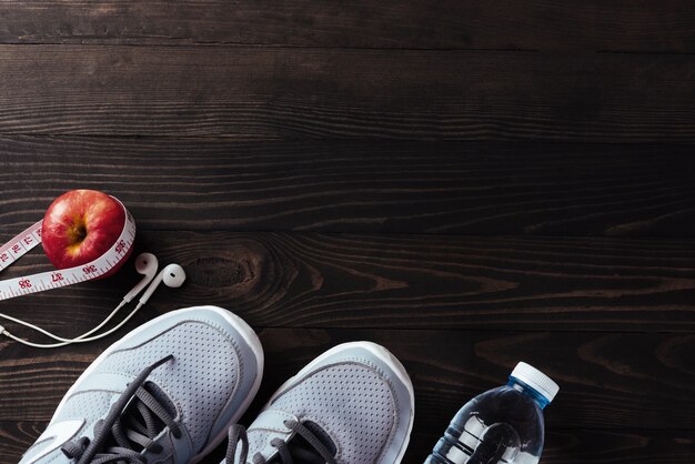 Paire de chaussures de sport, écouteurs, pomme et bouteille d'eau sur une table en bois noir