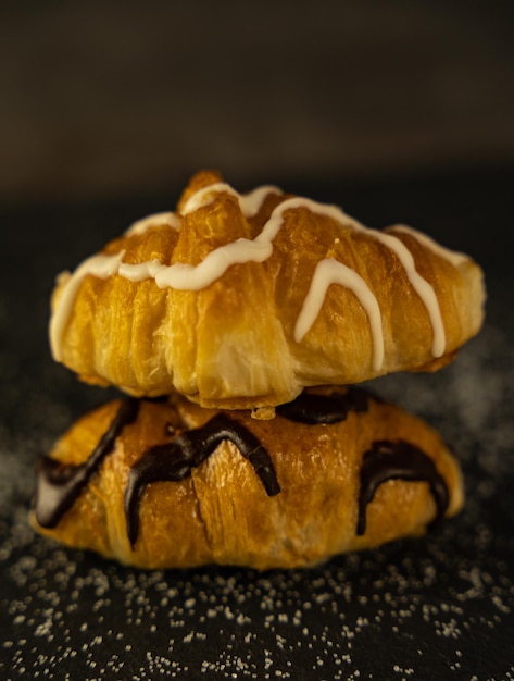 Paire de délicieux croissants au chocolat et sucre sur fond sombre