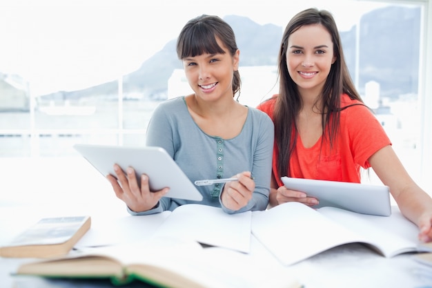 Une paire de filles souriantes qui travaillent avec des tablettes en regardant dans la caméra