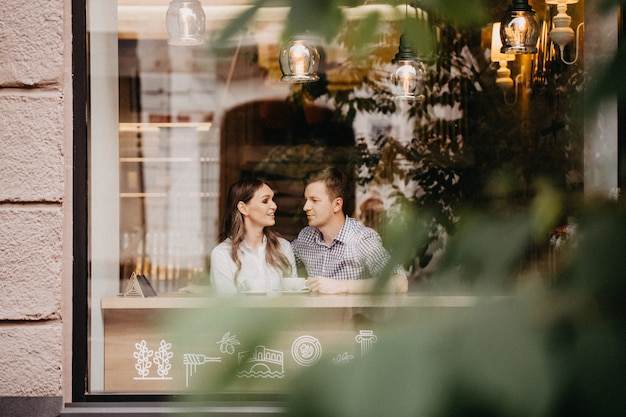 Paire de gens heureux assis et souriant au café derrière la vitre