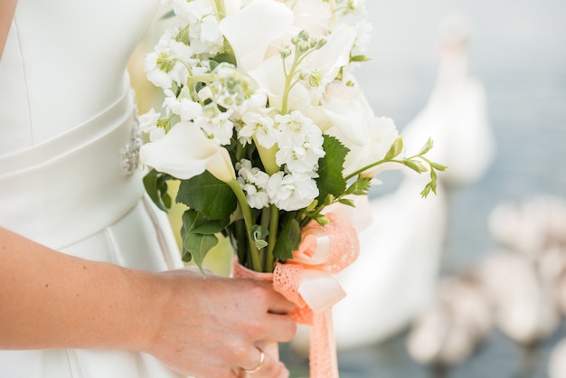 Une paire de jeunes mariés avec un bouquet de roses blanches se trouve près du lac. le cygne nage