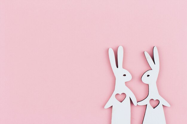 Une paire de lapins en bois blanc avec des coeurs dans leur poitrine sur un espace de copie de fond rose