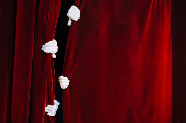 Photo paire de main de mime tenant un rideau rouge fermé