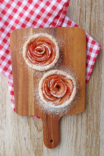 Paire de mini tartelettes en forme de rose pomme saupoudrées de sucre en poudre sur une planche à pain en bois