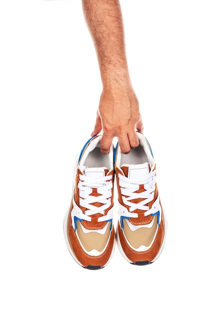 Photo paire de nouvelles chaussures ou baskets marron sans marque dans la main masculine isolée sur fond blanc avec un tracé de détourage
