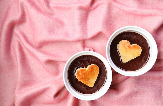 Paire de pâtisseries à la mousse au chocolat avec des gâteaux en mousseline de soie en forme de coeur sur un tissu drapé rose