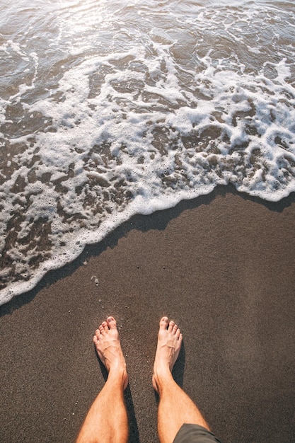 paire de pieds nus plantés fermement sur le sable noir partiellement immergé dans les douces vagues