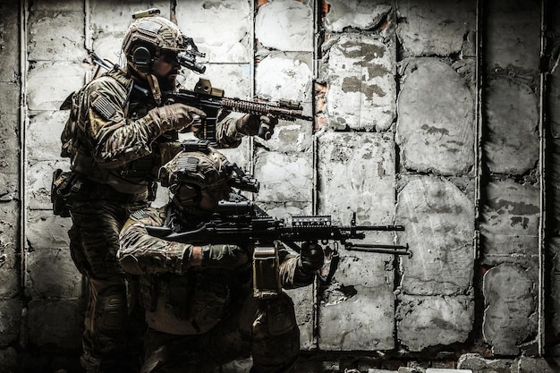 Paire de Rangers de l'armée avec fusil et mitrailleuse se déplaçant le long du mur de béton en mission. Ils sont prêts à commencer à tirer si l'ennemi apparaît. Prise de vue en extérieur