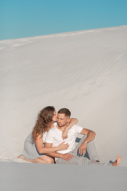 Paire romantique assis sur le sable blanc et huggins dans le désert