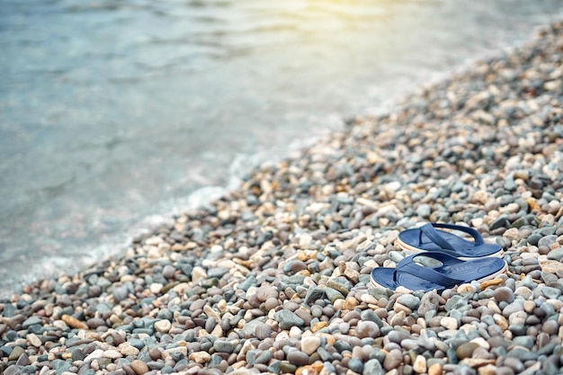 Paire de tongs bleu vif à gauche sur la plage de galets contre l'eau bleue floue