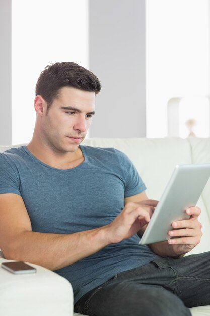 Paisible bel homme se détendre sur le canapé avec tablette