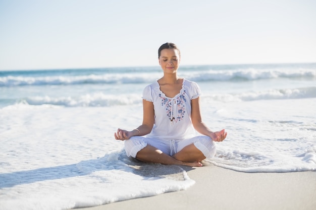 Paisible jolie femme en position du lotus sur la plage avec la vague qui l&#39;atteint