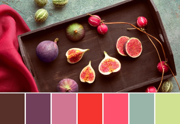 Palette de correspondance des couleurs d'automne d'automne de saison Fruits de figues frais coupés en deux sur un plateau en bois noir Foulard en soie rouge framboise et fruits déco sur une planche turquoise