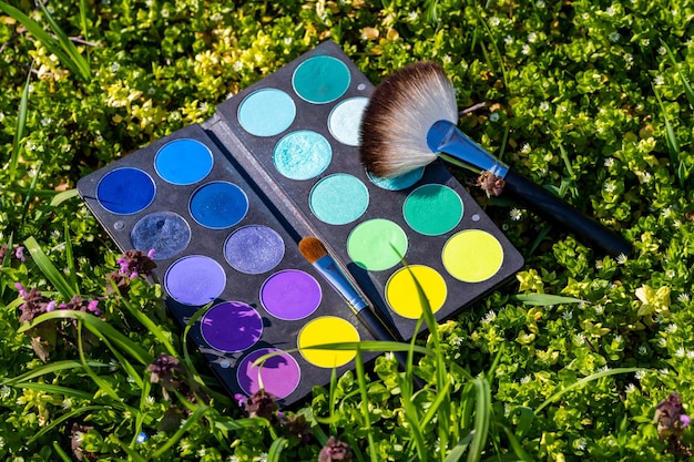 Une palette avec différentes couleurs et un pinceau dans l'herbe.