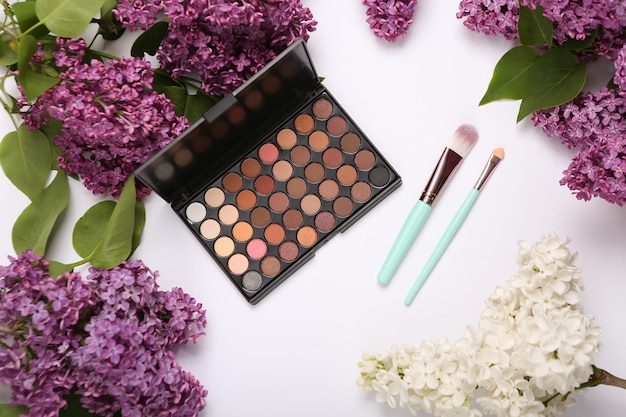 Palette de fards à paupières et pinceaux de maquillage avec des branches de lilas en fleurs sur fond blanc Concept de beauté de printemps Vue de dessus Mise à plat