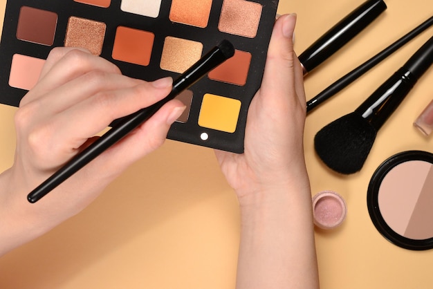 Palette d'ombres à paupières sur la main de la femme Produits de maquillage professionnels avec produits de beauté cosmétiques fond de teint rouge à lèvres ombres à paupières pinceaux et outils