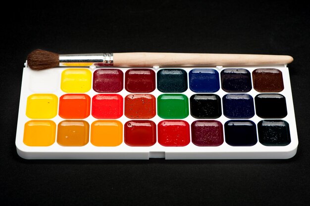 La palette de peintures à l'aquarelle et de pinceaux sur fond noir