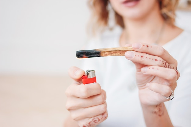 Palo santo ou Bursera graveolens. Blonde jeune femme lumières collent bois sacré, gros plan