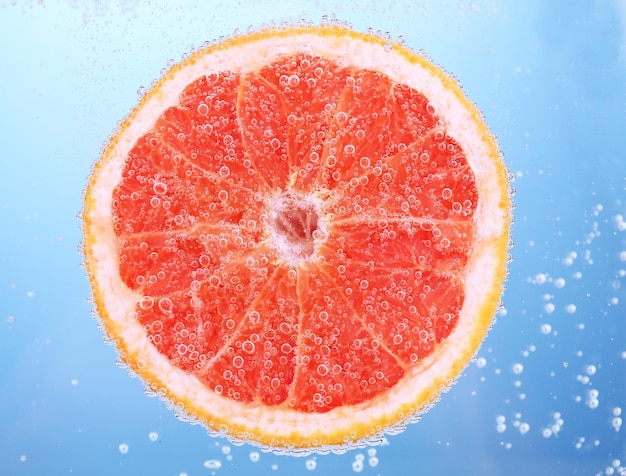 Pamplemousse frais dans l'eau avec des bulles sur fond bleu