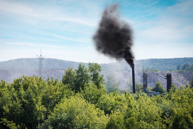 Photo panache de fumée de l'industrie émettant dans l'atmosphère sur fond d'arbres forestiers et ciel bleu. problème environnemental.