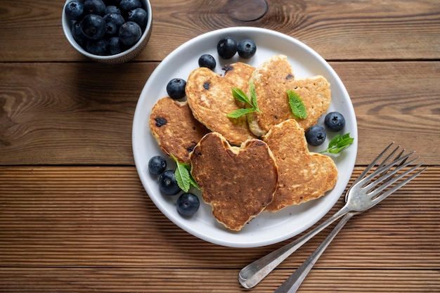 Pancakes en forme de coeur avec des myrtilles fraîches Petit-déjeuner matinal délicieuses crêpes végétaliennes Rustic woodenbackground