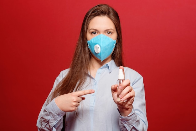 Pandémie de coronavirus, close-up portrait of young woman on red in medical protection mask sprays antiseptic