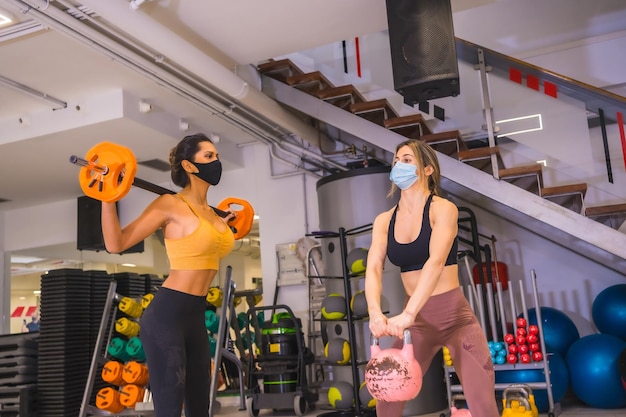 Pandémie de coronavirus dans les gymnases Deux filles s'entraînant avec des poids avec des masques faciaux