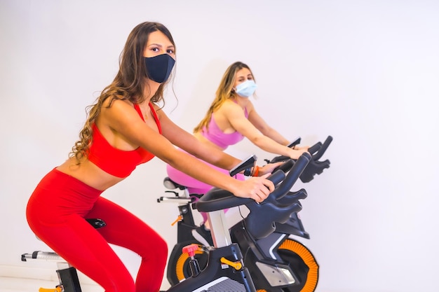 Pandémie de coronavirus dans les gymnases Deux filles s'entraînant sur des vélos avec des masques faciaux
