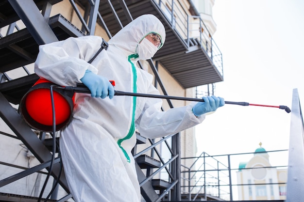 Pandémie de Coronavirus. Un désinfectant en tenue de protection et masque vaporise des désinfectants dans la maison ou au bureau. Protection contre la maladie COVID-19. Prévention de la propagation du virus de la pneumonie avec les surfaces.