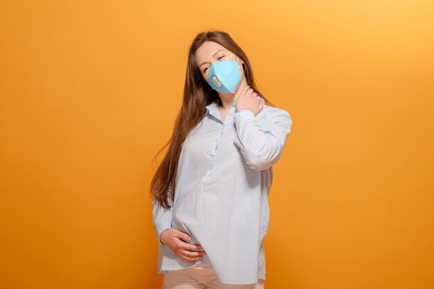 Pandémie de coronavirus, jeune femme enceinte sur jaune dans un masque médical de protection, douleur dans le cou