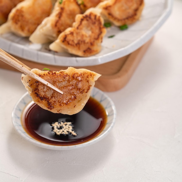 Panfried gyoza dumpling jiaozi dans une assiette avec de la sauce soja sur fond de tableau blanc