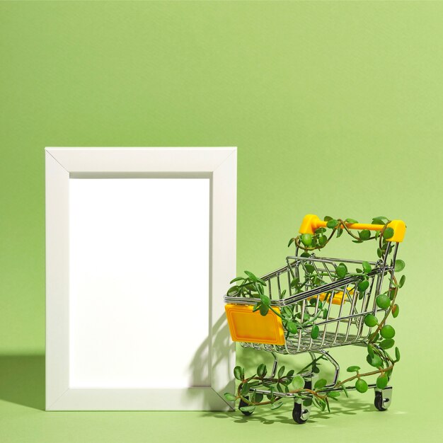 Panier d'achat entrelacé de plantes à côté d'un cadre de maquette vide sur fond vert consum...