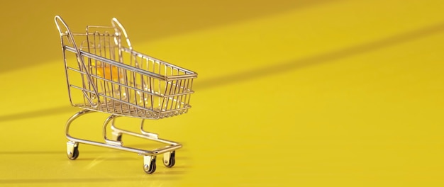 Panier d'achat sur fond clair jaune avec chariot de supermarché lumière du jour sur bannière publicitaire avec copie ...