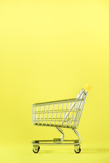 Panier d&#39;achat sur fond jaune. Chariot de magasin au supermarché. Concept de vente, discount, shopaholism. Tendance de la société de consommation